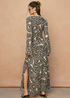 Woman wearing a long, patterned dress against a beige wall.