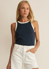 Woman wearing a navy sleeveless top with white trim and a white denim skirt on a beige background