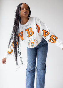  Person wearing a white long-sleeve shirt with orange text and blue jeans on a plain background