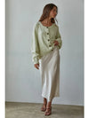 Woman wearing a light green cardigan and white skirt against a plain background