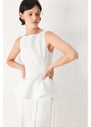 Woman wearing a white sleeveless top and pants on a light gray background