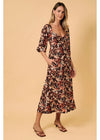 A woman modeling a midi-length floral dress with three-quarter sleeves and a V-neckline, set against a solid beige studio background.