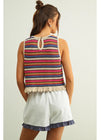 Woman wearing a colorful striped sleeveless top and white shorts on a plain background