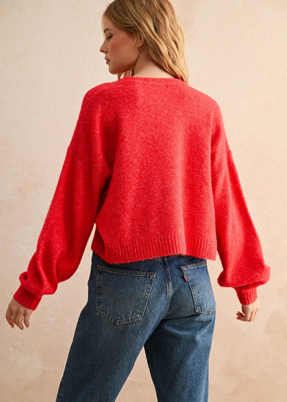 Person wearing a red sweater and blue jeans against a beige background