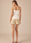 Woman wearing a white tank top and beige shorts on a beige background