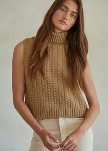 Woman wearing a beige knitted sleeveless sweater against a neutral background