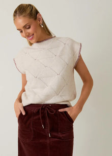  Woman wearing a beige quilted top and brown pants against a plain background