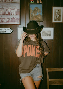  Person wearing a cowboy hat and 'POKER' shirt in a room with wooden walls and framed pictures.