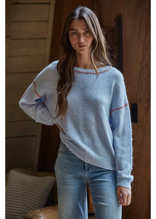  Woman wearing a light blue sweater with decorative sleeves in a warm-toned room.