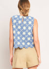 Woman wearing a sleeveless blue and white patterned top with beige shorts on a plain background