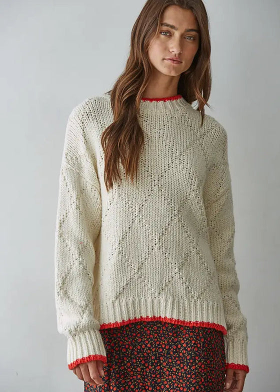 Woman wearing a cream knitted sweater with red trim against a plain background