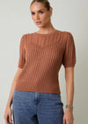 Woman wearing a brown knitted sweater and blue jeans against a plain background