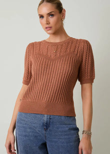  Woman wearing a brown knitted sweater and blue jeans against a plain background