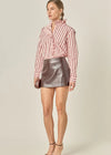 Woman wearing a pink and white striped shirt and metallic skirt on a beige background
