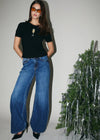Woman wearing a black top and blue jeans standing next to a decorated Christmas tree.