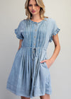 Woman wearing a light blue denim dress with ruffled sleeves on a gray background