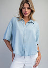 Woman wearing a light blue denim shirt and white pants on a gray background
