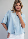 Woman wearing a light blue denim shirt and white pants against a gray background
