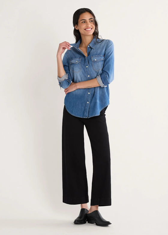 Woman wearing a blue denim shirt and black pants on a white background