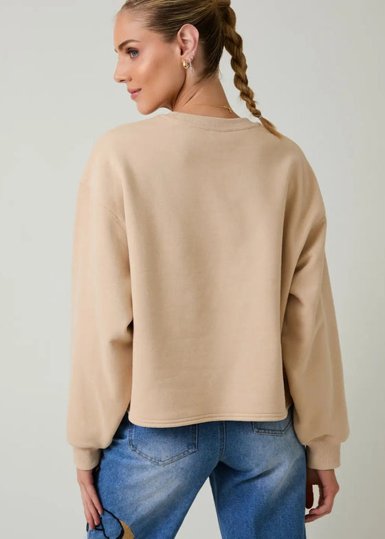 Woman wearing a beige sweatshirt and blue jeans on a plain background