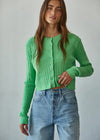 Woman wearing a green knitted cardigan and blue jeans against a plain background