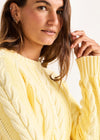 Woman wearing a yellow cable knit sweater against a white background