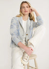 Woman wearing a light blue and gray cardigan sitting on a stool against a white background