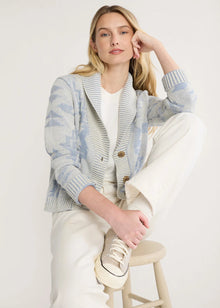  Woman wearing a light blue and gray cardigan sitting on a stool against a white background