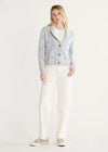 Woman wearing a light blue cardigan over a white shirt with white pants on a plain background