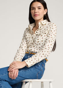  Woman wearing a floral blouse and blue jeans sitting on a white chair against a light gray background
