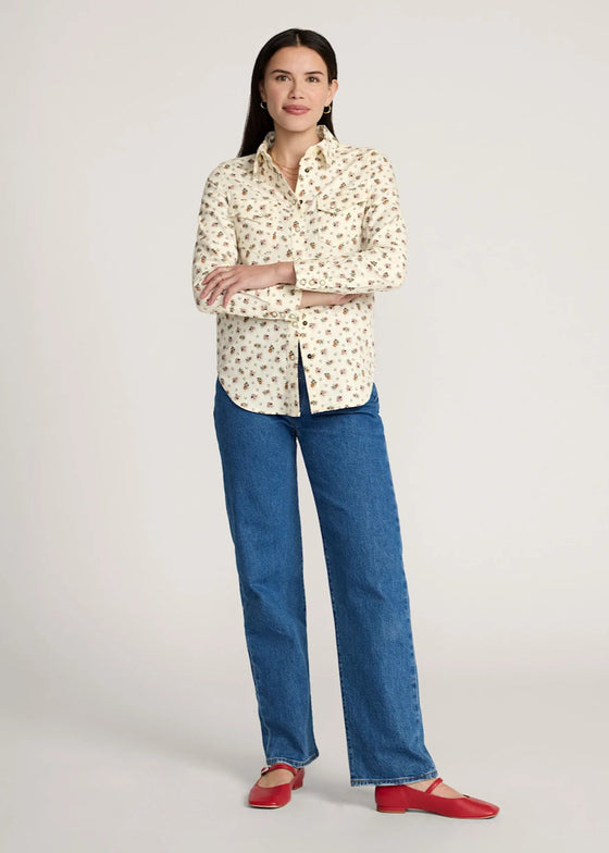 Woman wearing a patterned blouse, blue jeans, and red shoes on a white background