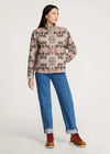 Woman wearing a patterned shirt, blue jeans, and brown boots on a white background