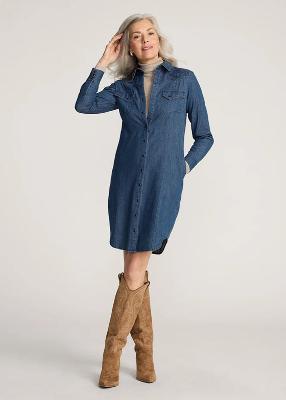 Woman wearing a blue denim dress and brown knee-high boots on a plain background