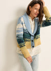 Woman wearing a colorful knitted cardigan with landscape design against a plain background