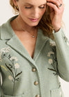 Woman wearing a green coat with floral embroidery on a white background