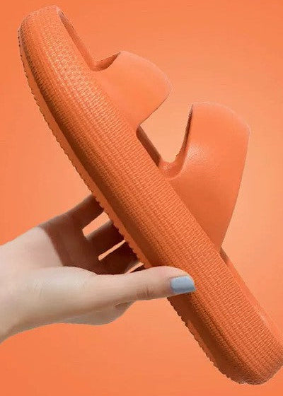 Orange sandal held by a hand against an orange background