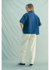 Person wearing a blue denim shirt and beige pants on a light green background