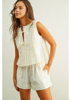 Woman wearing a white sleeveless top and shorts on a plain background