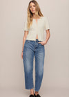 Woman wearing a beige top and blue jeans against a plain background