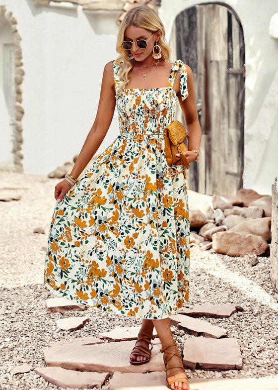 Woman in a floral dress standing on a rocky beach.