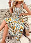 Woman wearing a floral dress sitting on a stone path with a woven bag and flowers.