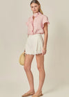 Woman wearing a pink blouse and white shorts with a beige background