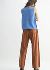 Person wearing a blue sleeveless top and brown pants on a white background