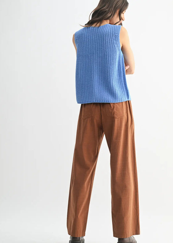 Person wearing a blue sleeveless top and brown pants on a white background