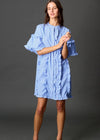 Woman wearing a blue dress with ruffled sleeves against a gray background