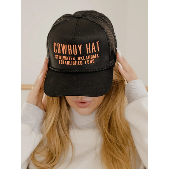 Black cap with text worn by a person on a neutral background