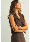 Woman wearing a brown sleeveless vest over a dress against a light background
