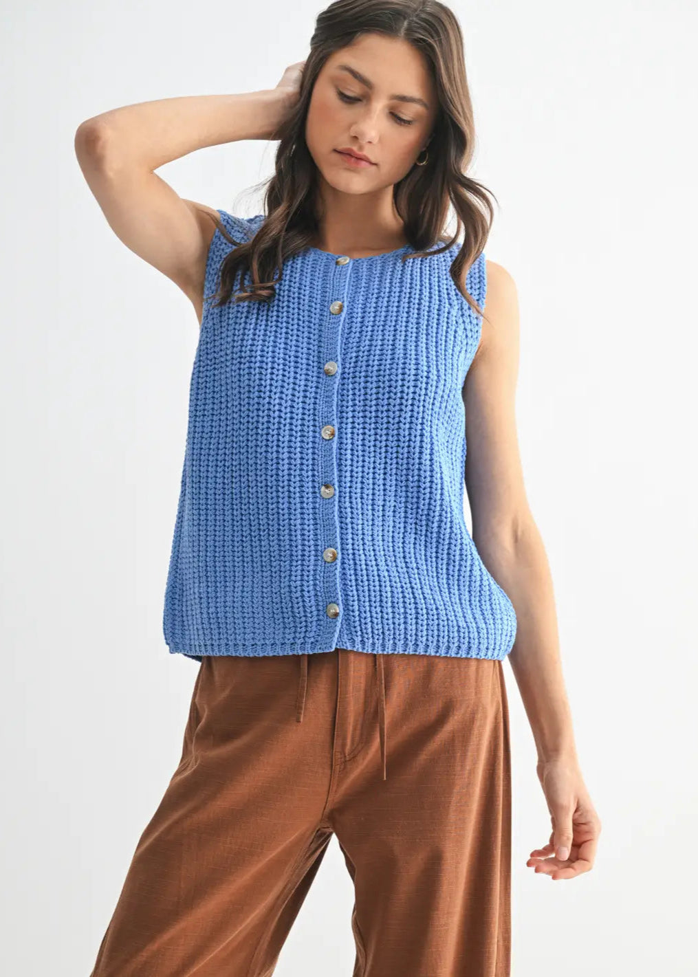  Woman wearing a blue knitted sleeveless top with brown pants on a white background