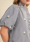 Close-up of a person wearing a black and white striped shirt with floral embroidery on a beige background