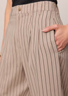 Beige pinstripe pants with a hand on the pocket against a neutral background